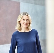 Susann Senkpiel steht freundlich lächelnd im Gräfin-Dönhoff-Gebäude vor der roten und blauen Betonwand. ©Tobias Tanzyna