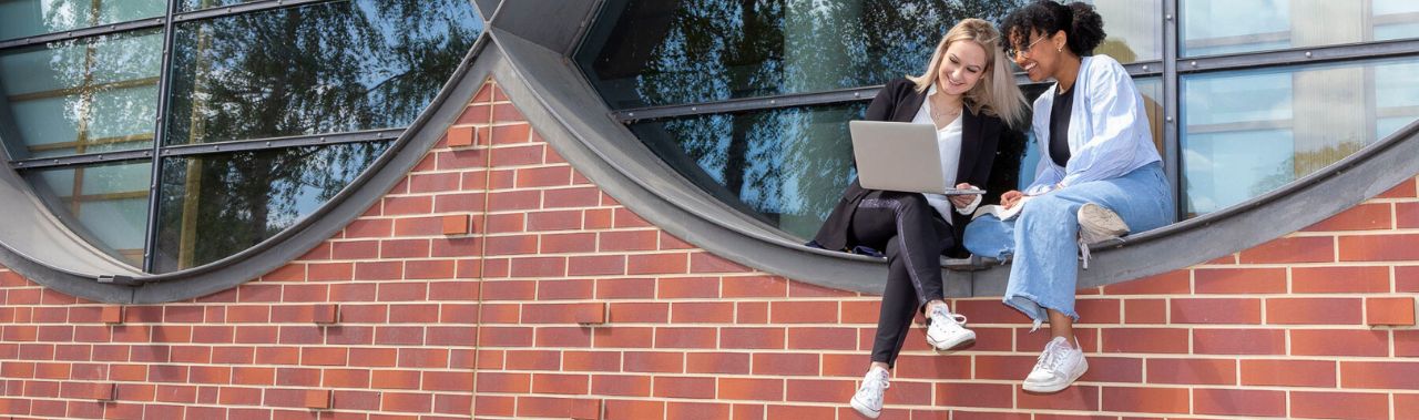 Studentinnen blicken auf einen Laptop und studieren das Studierendenangebot