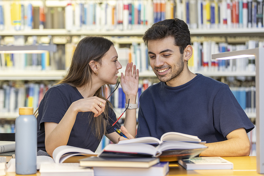 Studierende unterhalten sich und lesen Bücher in der Bibliothek Studierende unterhalten sich und lesen Bücher in der Bibliothek